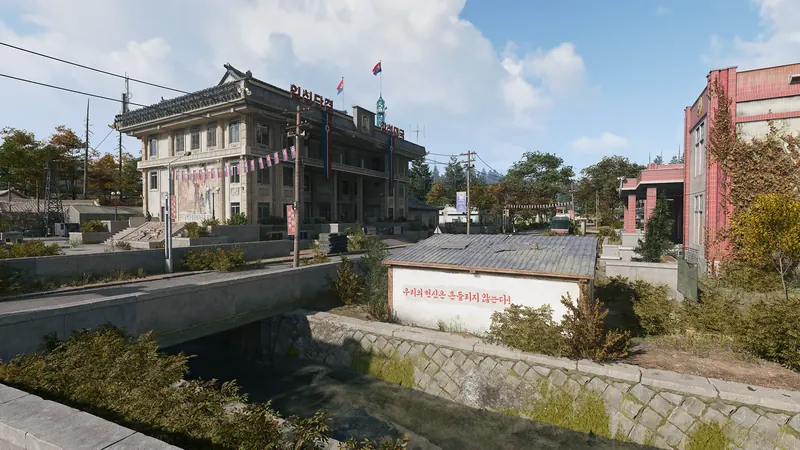 North Korean government building decorated with flags and propaganda banners beside a canal and concrete bridge.