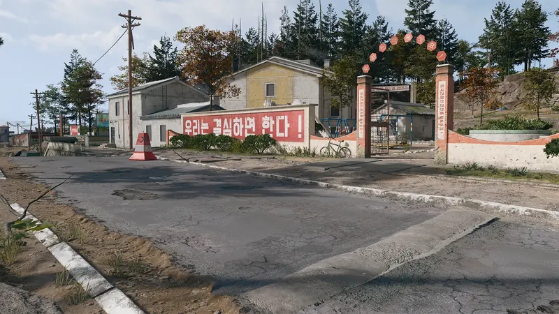 Village entrance with Korean slogans painted on walls, a gated courtyard, and small buildings surrounded by trees.